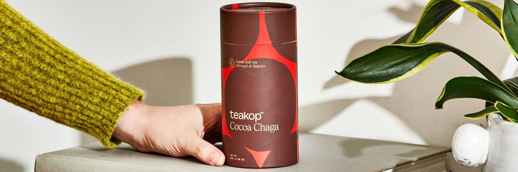 A hand reaching for a tin of teakop Cocoa Chaga